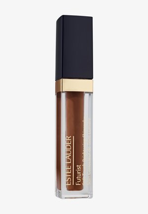 Correcteur liquide Estée Lauder Futurist en brun moyen avec un bouchon noir et une bordure dorée sur fond blanc.