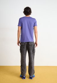 Purple cotton T-shirt, gray cargo pants with multiple pockets and a faded texture, paired with blue and black chunky sneakers.