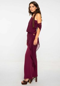Vestido burdeos con un diseño fluido, corte off-shoulder y choker decorativo marrón. Presenta una tela texturizada y un dobladillo asimétrico.