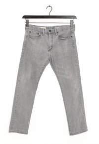 Jeans de mezclilla gris con corte recto, cinco bolsillos y una ligera textura desgastada. Cuenta con una etiqueta en la cinturilla y presillas para el cinturón. Cuelga de una percha negra.