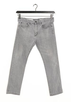 Šedé džíny z denimu se střihovým střihem, pěti kapsami a mírným vybledlým povrchem. Obsahují štítek na pásku a poutka na opasek. Visí na černém ramínku.