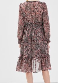 Robe noire transparente avec un motif abstrait rose et blanc, taille smockée, manches longues et ourlet à volants. Tissu léger et fluide.
