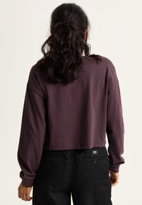 Korte, lange mouwen top van donkerpaarse katoen. Heeft een eenvoudig ontwerp met een ronde halslijn en een rechte zoom. Gekocht met zwarte broek.