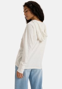 Sweatshirt à capuche beige clair en tissu doux avec des manches longues. Coupe ample, ourlet arrondi et style décontracté associé à un jean bleu clair.