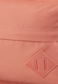 Bolsa de tela color durazno con superficie texturizada, con un acento en forma de diamante y detalles cosidos. Cierre con cremallera y bolsillo lateral.