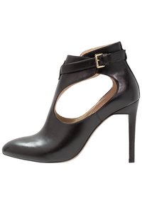 Černá kožená kotníková bota s špičatou špičkou, otevřenými stranami a jedním přezkovým popruhem. Disponuje lesklým povrchem a jehlovým podpatkem.