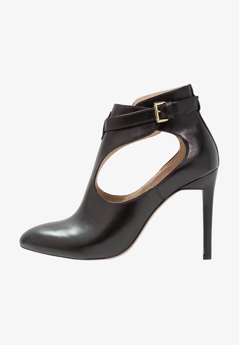 Černá kožená kotníková bota s špičatou špičkou, otevřenými stranami a jedním přezkovým popruhem. Disponuje lesklým povrchem a jehlovým podpatkem.
