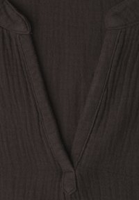 Gros plan sur un tissu texturé brun foncé avec un col en V profond et des détails de couture visibles.