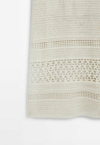 Tissu crème au crochet avec des rayures horizontales alternant points serrés et ouverts, montrant des motifs de dentelle détaillés sur un fond blanc.