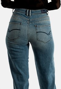 Vaqueros de mezclilla con un lavado azul claro, diseño de cinco bolsillos y costuras en contraste. La parte trasera cuenta con dos bolsillos en ángulo con costuras decorativas.