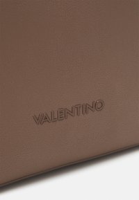 Brun läderhandväska med det präglade varumärket "VALENTINO" i matchande färg, med en mjuk textur och minimalistisk design.