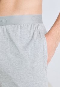 Boxer shorts din bumbac gri, cu un elastic în talie și branding embosat "Calvin". Materialul are o textură netedă și o croială lejeră.