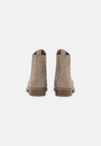 Bottines en daim beige avec panneaux élastiques sur les côtés, un petit talon empilé, et des détails de couture ton sur ton. Texture lisse et design minimaliste.