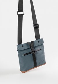 Graue Leder-Umhängetasche mit Klappe, schwarzem Riemen, Reißverschlusstasche und braunem Boden. Verfügt über einen Schnallenverschluss und ein geprägtes Logodetail.