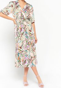 Sukienka midi w kwiatowy wzór z designem typu wrap, krótkimi podwiniętymi rękawami i elastyczną talią. Kolory to pastelowy róż, zieleń i niebieski.
