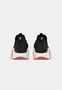 Et par sorte og hvide Nike sneakers med røde såler vist fra bagsiden på en ensfarvet lys baggrund.