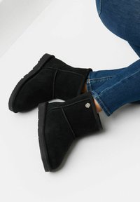 Stivali alla caviglia in suede nero con finitura testurizzata, suola piatta in gomma e cuciture laterali, caratterizzati da un piccolo accento di logo metallico.