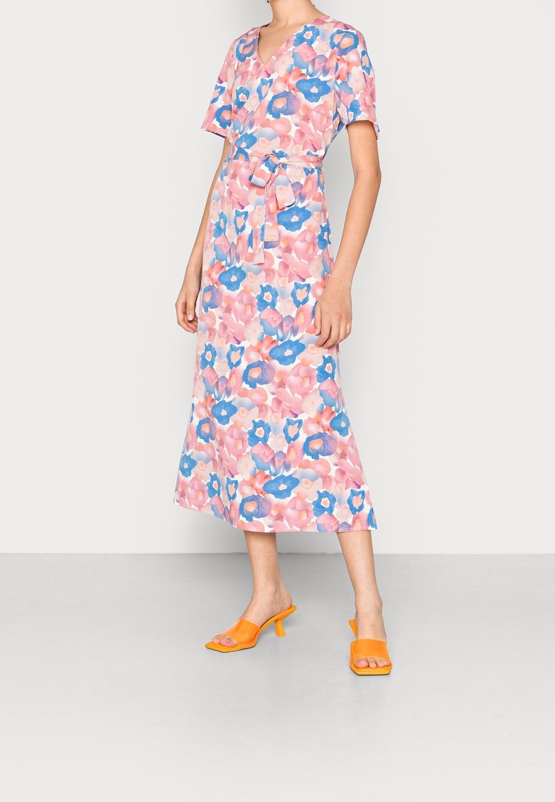 Blumen-Midi-Kleid in Pink, Blau und Creme, mit kurzen Ärmeln und einem gebundenen Taillengürtel. Kombiniert mit orangefarbenen, hochhackigen Sandalen. Weiche Textur.