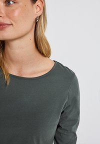Langermige, donkergroene shirt met een ronde halslijn, gemaakt van zachte stof, met gestikte details langs de kraag en mouwen.
