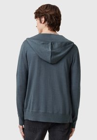 Felpa blu scuro con maniche lunghe, cappuccio con cordino e polsini a coste. Il tessuto sembra leggero e liscio al tatto.