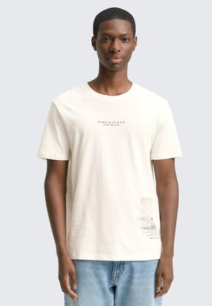 Korte mouwen crème t-shirt van katoenmateriaal, geprinte tekst op de voorkant, klein logopatch aan de zoom, relaxte pasvorm, ronde halslijn, lichte textuur.