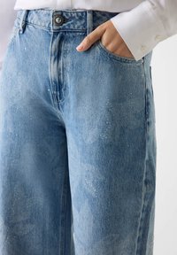 Hele sinised teksapüksid kõrge vöökohaga, sirge lahjusega ja peente lehemustritega. Omavad nupuga sulgemist ja küljetaskuid.