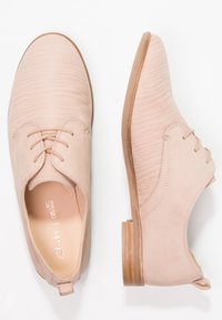 Chaussures en cuir rose clair avec une surface texturée, un design à lacets, un bout rond et un talon en bois. Elles comportent une languette à l'arrière.
