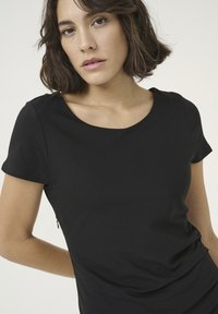 Haut noir à manches courtes avec encolure dégagée, fabriqué en tissu lisse et extensible. Présente une coupe slim avec un détail de couture latérale discret.