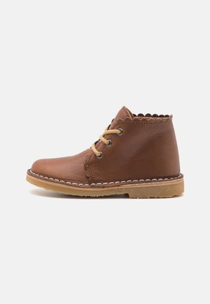 Brune lær ankelsko med scalloped krave, beige snørebånd og hvit sømdetalj. Gummisåle med subtil tekstur. Sidevisning.