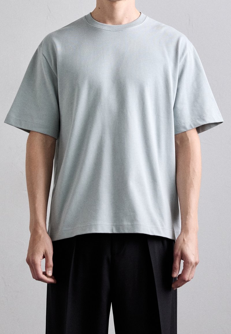 Světle modré bavlněné tričko s krátkým rukávem a kulatým výstřihem. Volný střih s minimem švů, s hladkou texturou a čistými liniemi.