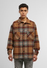 Bruine geruite flanellen shirt met een kraag, twee borstzakken en zwarte knopen; heeft een mix van beige, rood en witte strepen met een zachte textuur.