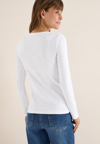 Langærmet hvid bomulds skjorte med rund halsudskæring, glat tekstur og tætsiddende design. Sammen med blå denimjeans.