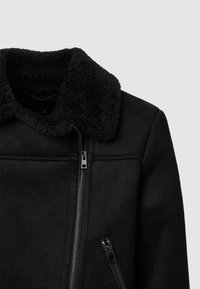 Giacca nera con un colletto in shearling testurizzato, zip frontale e tasca laterale con zip; presenta un tessuto liscio e linee pulite.