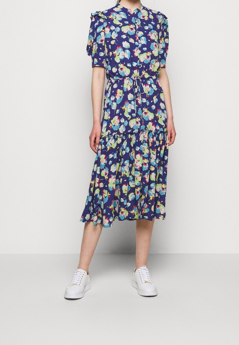 Květinové midi šaty v námořnické modři s krátkými nabíranými rukávy, zapínáním na knoflíky a sukňovým volánem. V kombinaci s bílými teniskami pro ležérní vzhled.