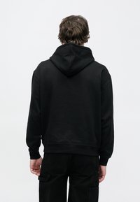 Μαύρο βαμβακερό φούτερ με απαλό ύφασμα, μπροστινή τσέπη, και ρυθμιζόμενο κορδόνι στην κουκούλα, με ριμπ μανσέτες και τελείωμα, απεικονίζεται από πίσω.