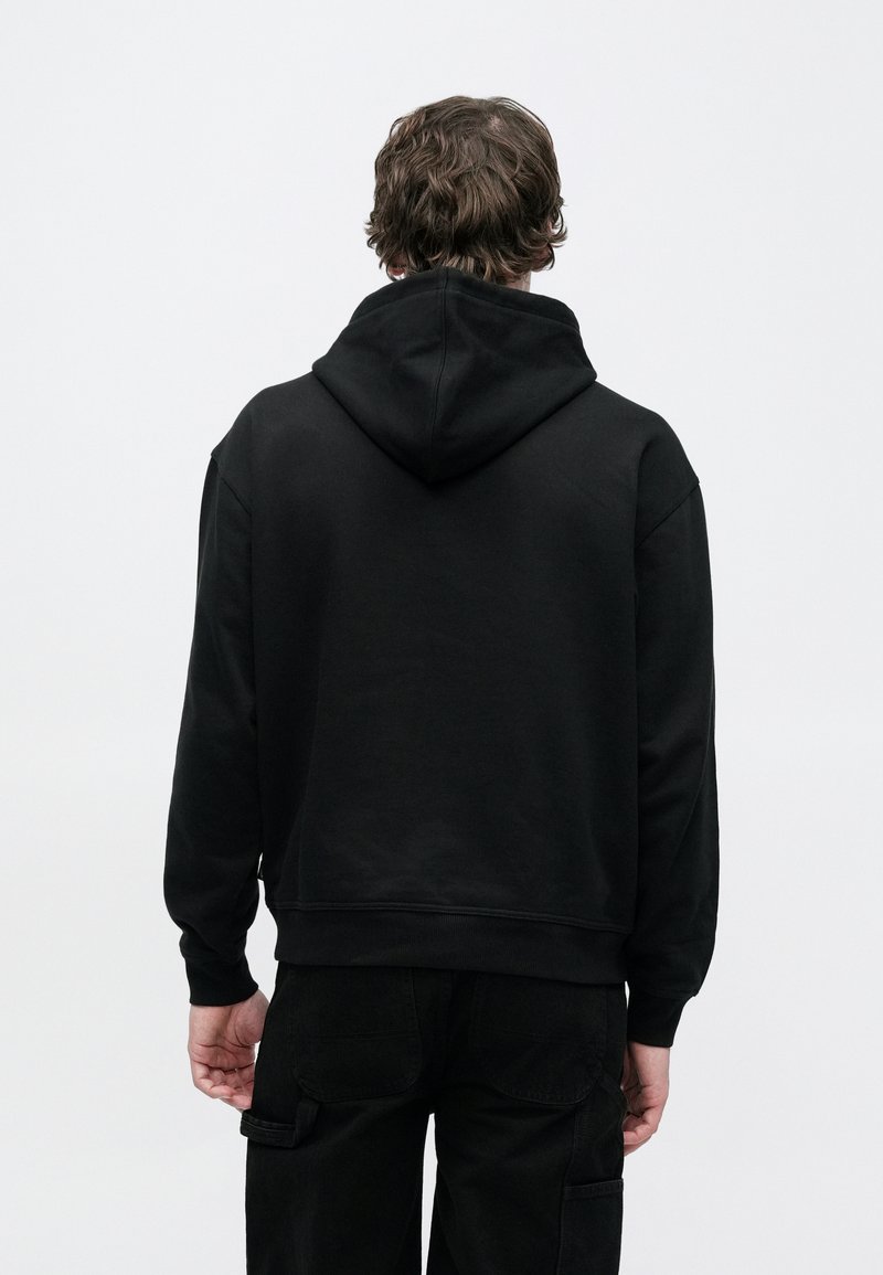 Sudadera con capucha de algodón negro que presenta una textura suave, bolsillo frontal y capucha con cordón ajustable, con puños y dobladillo acanalados, vista desde atrás.