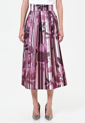 Femme portant une jupe midi plissée à rayures verticales et imprimé floral abstrait violet, associée à des talons hauts argentés.