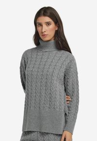 Grauer Kabelstrickpullover mit geripptem Rollkragen, lockerer Passform und seitlichen Schlitzen. Ausgestattet mit strukturiertem Muster und langen Ärmeln. Weiche Wollmischung.