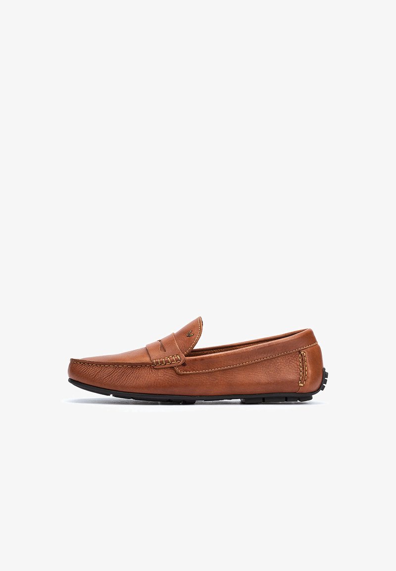 Mocasin de cuero marrón con un diseño cosido, punta redondeada y suela de goma. Presenta una tira en contraste sobre el empeine. Textura suave.