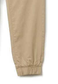 Beige joggerbroeken van lichtgewicht stof, met elastische boorden bij de enkels en een zachte textuur met minimale naden.