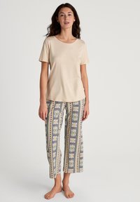 Beige short-sleeve shirt made of smooth fabric paired with patterned, loose-fit pajama pants featuring floral and geometric designs in pastel colors.