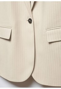 Blazer beige à fines rayures avec une fermeture à un bouton noir et deux poches à rabat à l'avant.
