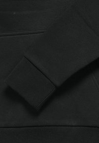 Manche de sweat-shirt noire avec poignet côtelé reposant sur la zone de la poche ventrale du vêtement.