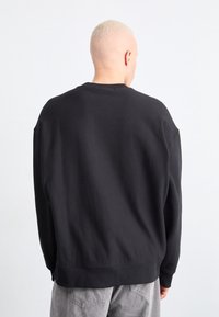 Zwarte sweatshirt in een katoenmix, oversized pasvorm, ribbels bij de mouwen en onderkant, weergegeven van achteren met een effen ontwerp en minimale details.