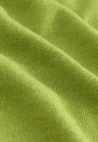 Gros plan sur un tissu tricoté doux et vert clair montrant une texture fine de points et des plis délicats.