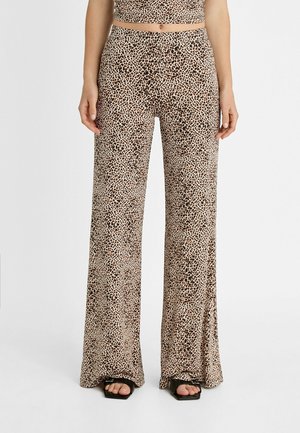 Femme portant un pantalon taille haute à jambes larges avec un imprimé léopard marron et noir, associé à des sandales noires à bouts ouverts.