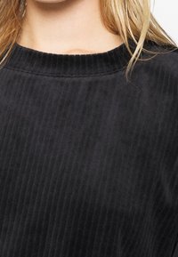 Felpa nera a costine con scollatura rotonda e tessuto morbido e testurizzato. La superficie presenta sottili linee verticali per un ulteriore dettaglio.