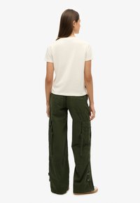 T-shirt blanc cassé à manches courtes associé à un pantalon cargo vert olive avec plusieurs poches et des zips latéraux pour un ajustement.