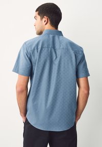 Chemise à manches courtes bleue avec un motif géométrique, dotée d'un col boutonné et d'un ourlet droit, confectionnée dans un tissu léger.