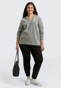 Gray patterned sweater with a V-neck, paired with black trousers. Model holds a black handbag and wears white sneakers.